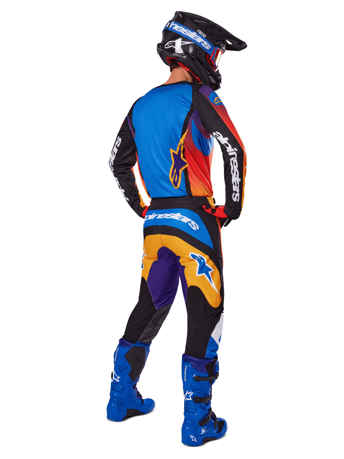 Pilote de motocross vu de dos portant le pantalon Alpinestars 2025 Fluid Wurx, design multicolore avec des accents bleus, orange, jaunes et violets, associé à un maillot assorti, des bottes bleu vif et un casque noir, équipement complet de course tout-terrain