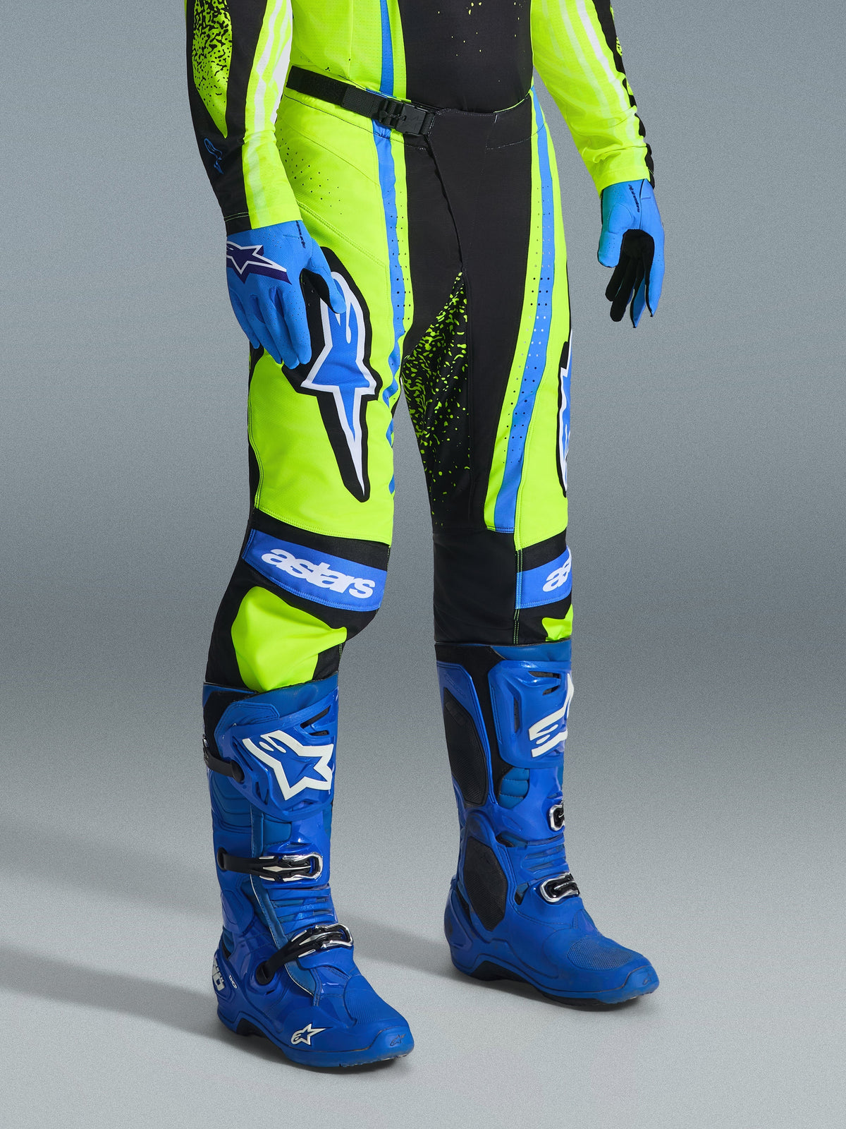 Alpinestars 2026 Techstar Nomur Pants, pantalon de motocross, jaune fluo, bleu marine et bleu UCLA, porté avec des bottes et des gants bleus assortis, logos blancs et panneaux renforcés, tenue de course professionnelle tout-terrain