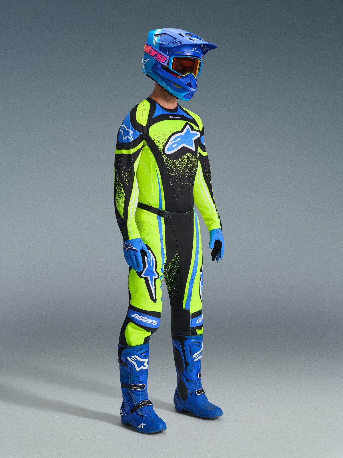 Pilote de motocross portant une tenue de course complète, maillot jaune fluo avec des accents bleu marine et bleu, pantalon Alpinestars 2026 Techstar Nomur aux couleurs assorties, casque bleu avec lunettes, bottes bleues et noires, gants bleus, tenue coordonnée pour la course tout-terrain