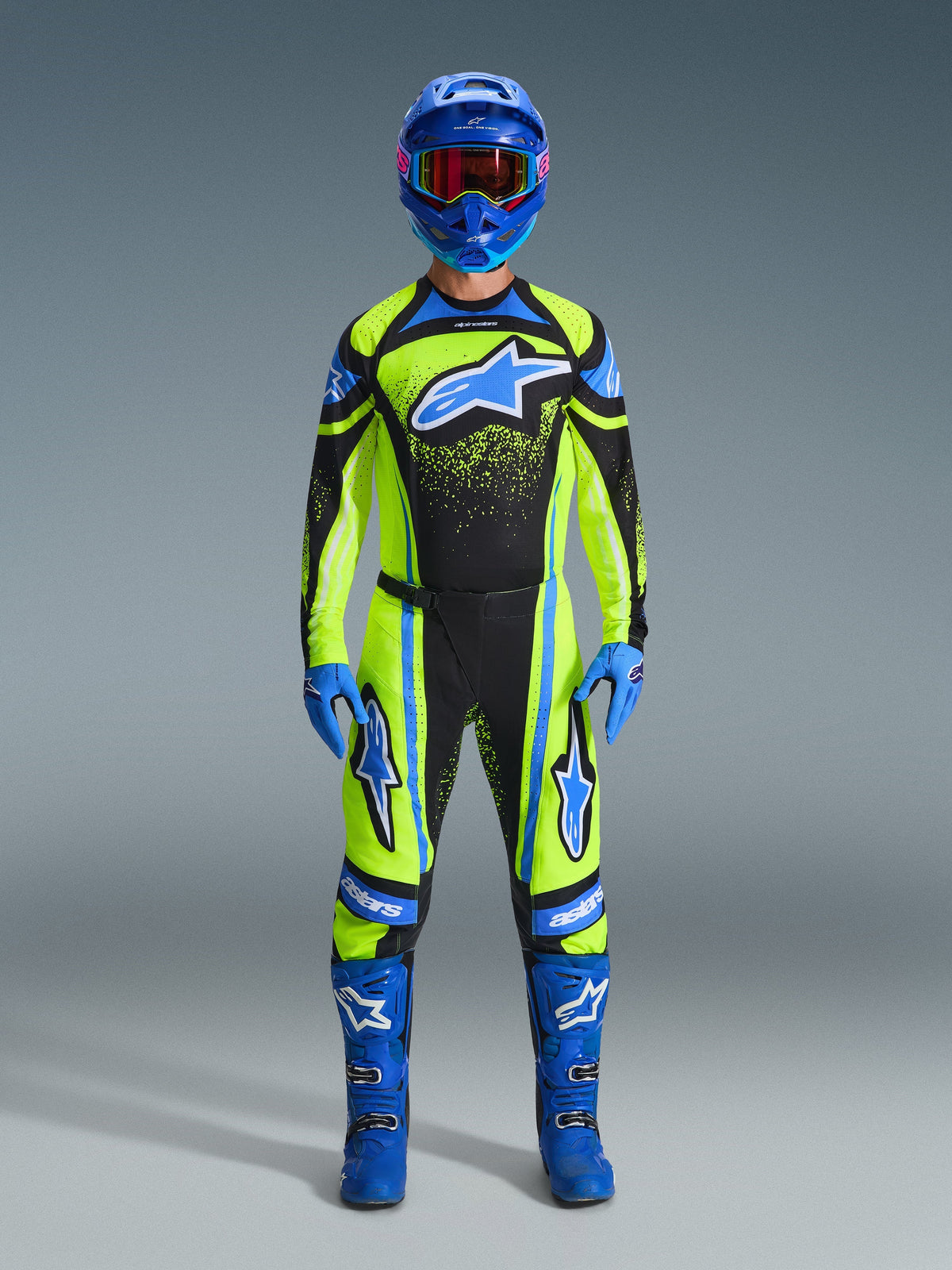 Pilote de motocross portant un équipement de course complet, pantalon et maillot Alpinestars Techstar Nomur 2026 jaune fluo et bleu marine avec des accents bleus, assorti d'un casque, de gants et de bottes bleus pour un look tout-terrain coordonné.