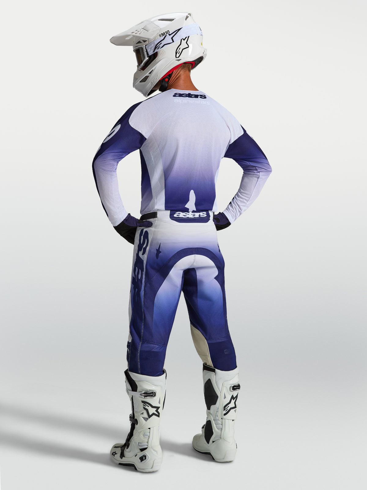 Alpinestars Racer Air Amber, pantalon de motocross pour homme, bleu et blanc, construction perforée à haut flux d'air, vue de dos sur un pilote avec bottes et casque blancs