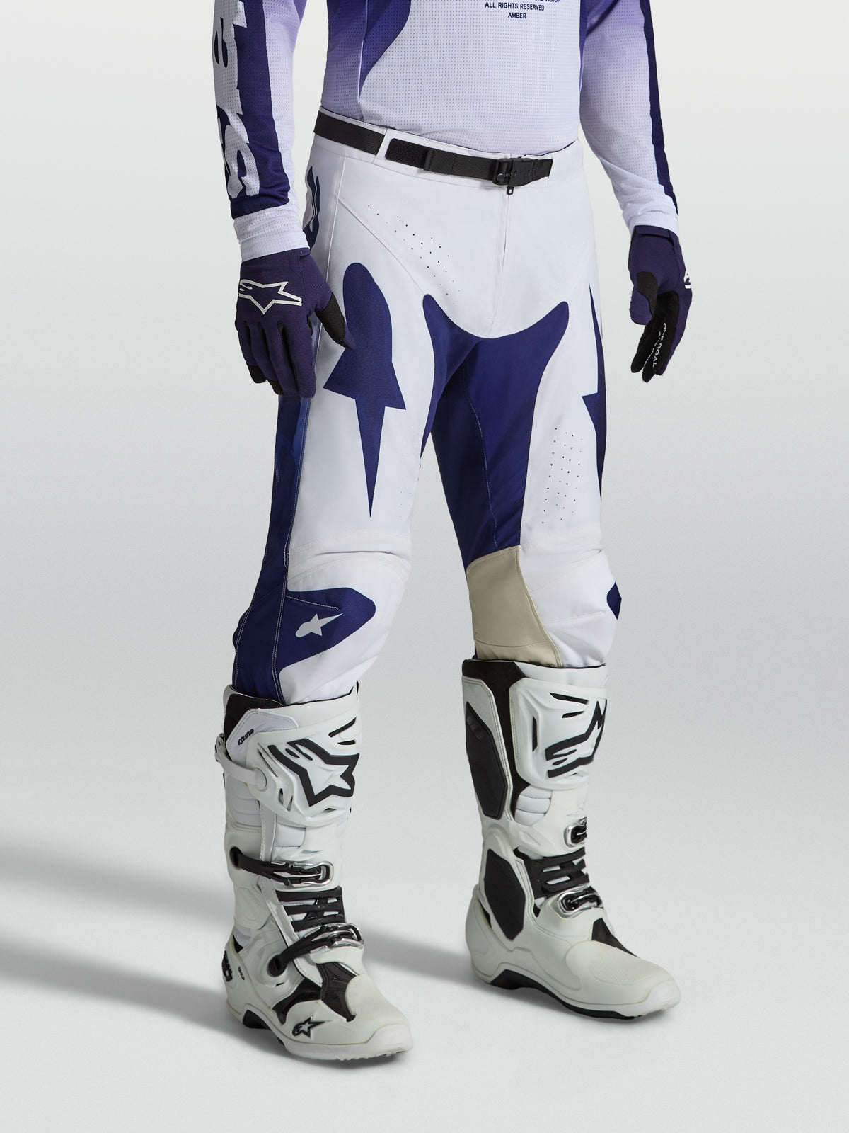 Alpinestars pantalon Racer Air Amber, pantalon de motocross pour homme, bleu et blanc, polyfibre perforée et coupe de course pré-courbée, porté avec des bottes de moto blanches.