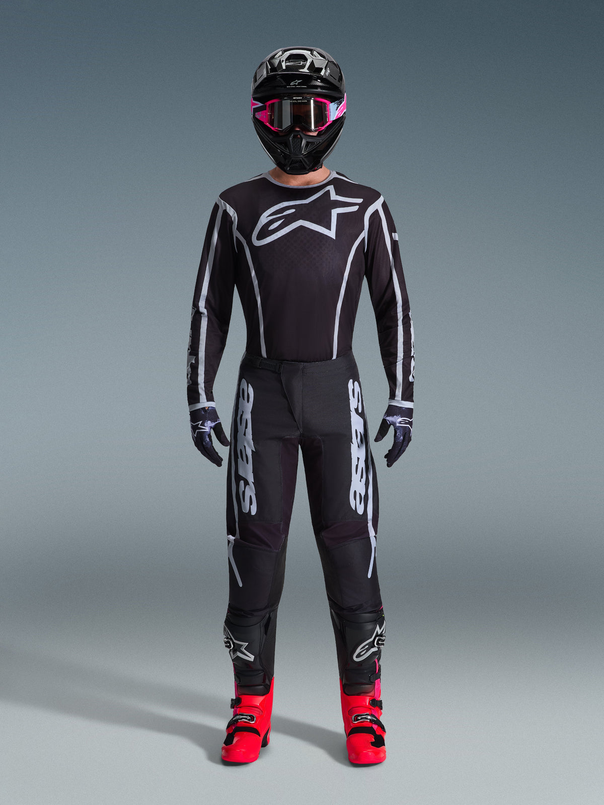 Ensemble Alpinestars 2026 Fluid Apex, tenue de motocross, noir avec accents gris, maillot arborant un grand logo Astars blanc, pantalon assorti avec un marquage imposant, casque noir avec lunettes roses et bottes rouge vif, kit complet de course tout-terrain