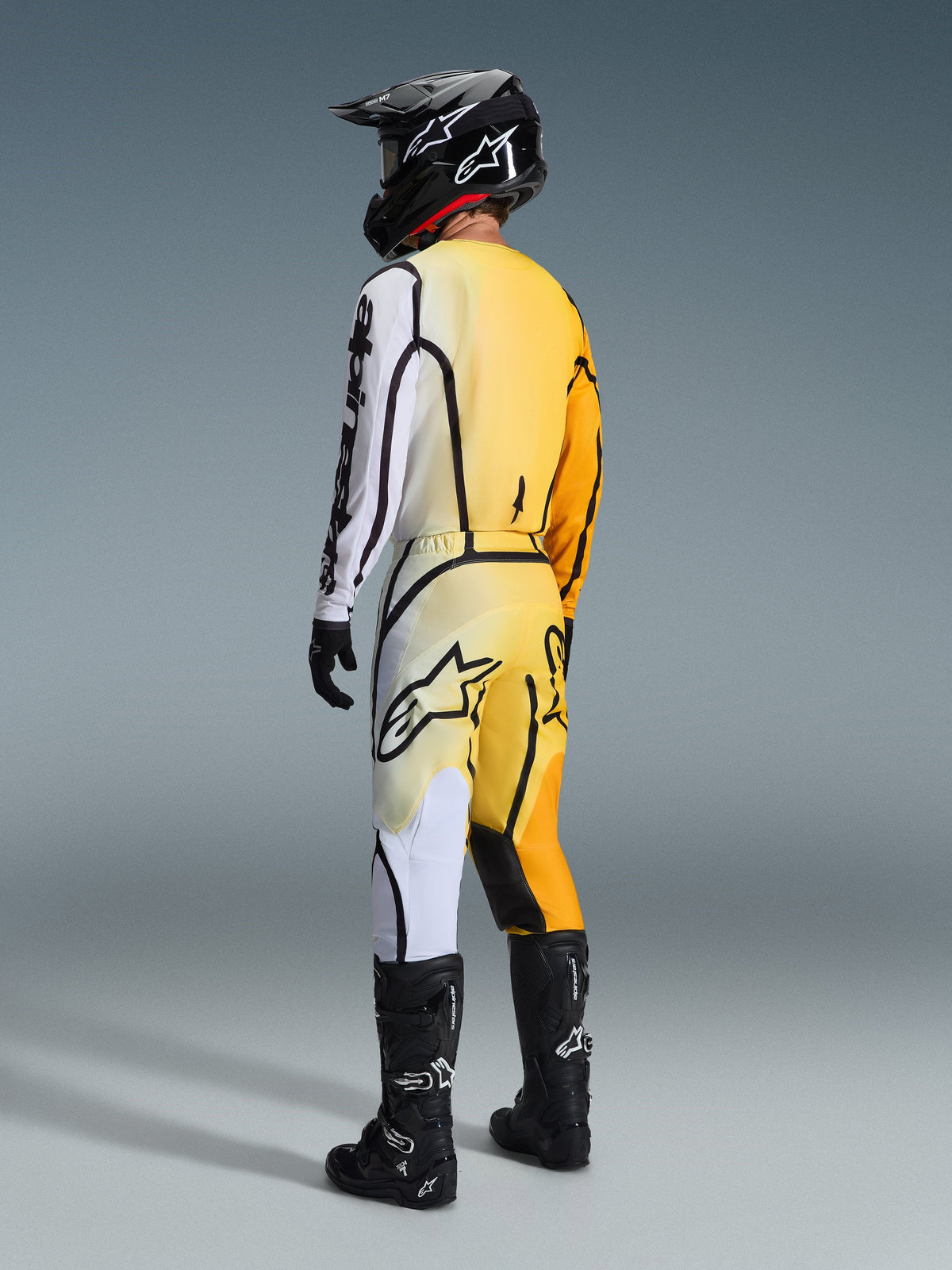Alpinestars 2026 Fluid Apex Pants, Motocross Pants, Yellow and White gradient with black accents, back view of rider in full racing gear including matching jersey, black helmet, and black boots
