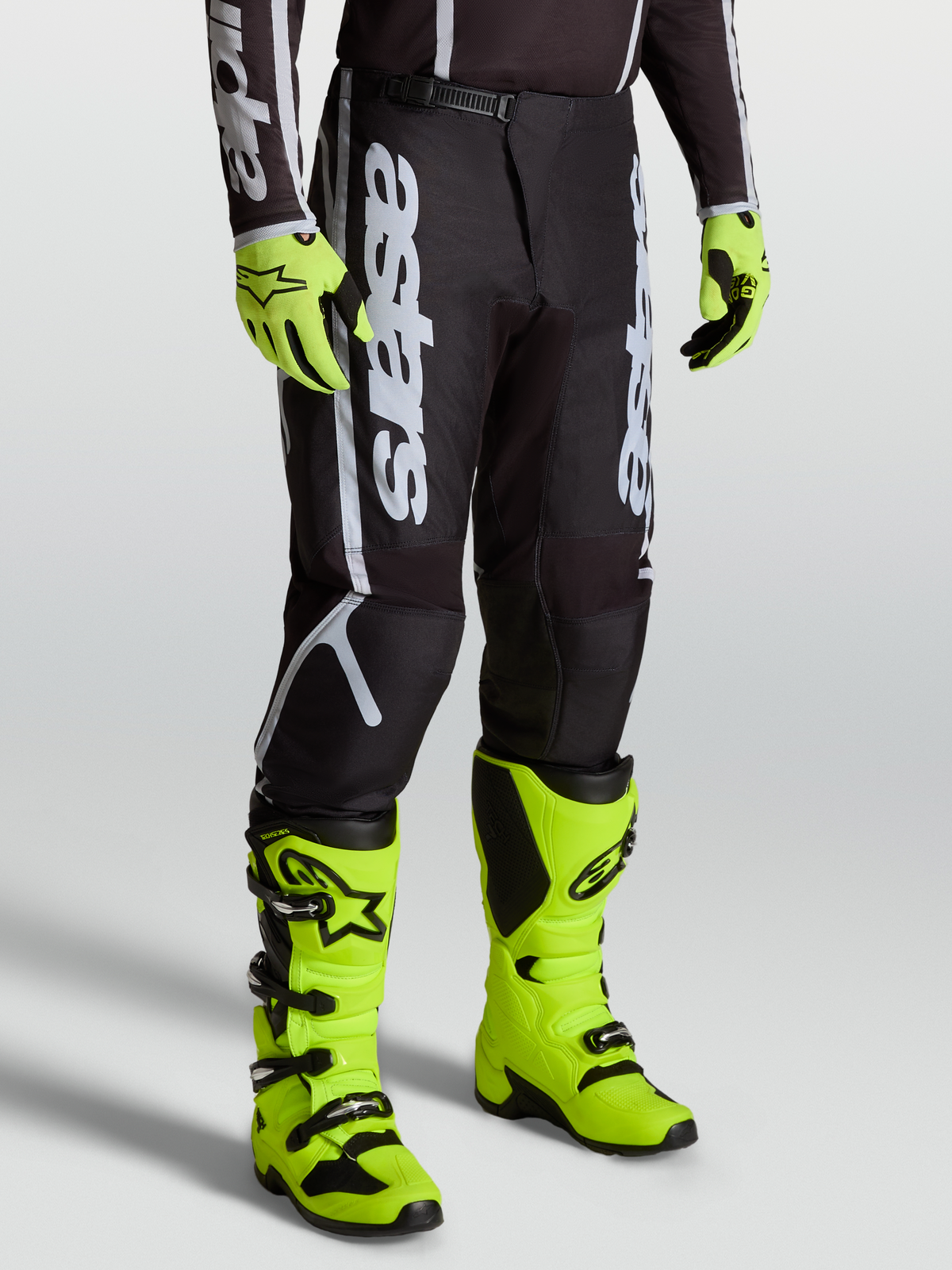 Alpinestars Pantalon Fluid Apex V2, équipement motocross homme, noir et argent, porté avec des bottes jaune fluo.