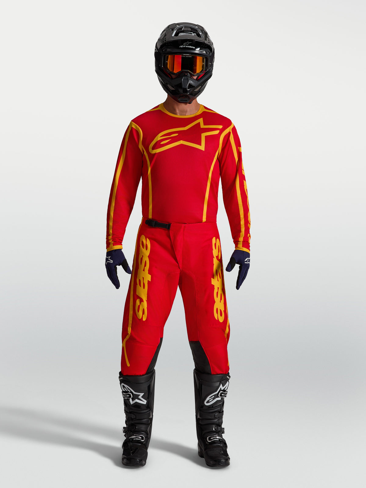Pantalon Alpinestars Fluid Apex V2, pantalon de motocross tout-terrain rouge et doré, porté avec maillot assorti et bottes.