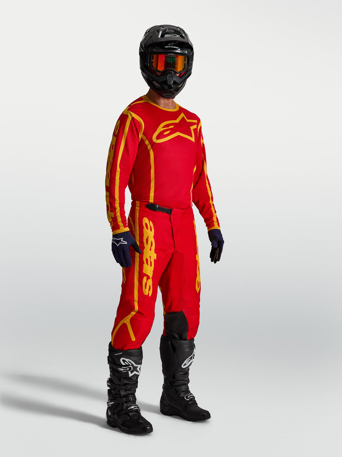 Pantalon Alpinestars Fluid Apex V2, équipement de motocross, rouge et doré, sur mannequin avec maillot et bottes pour une performance tout-terrain.