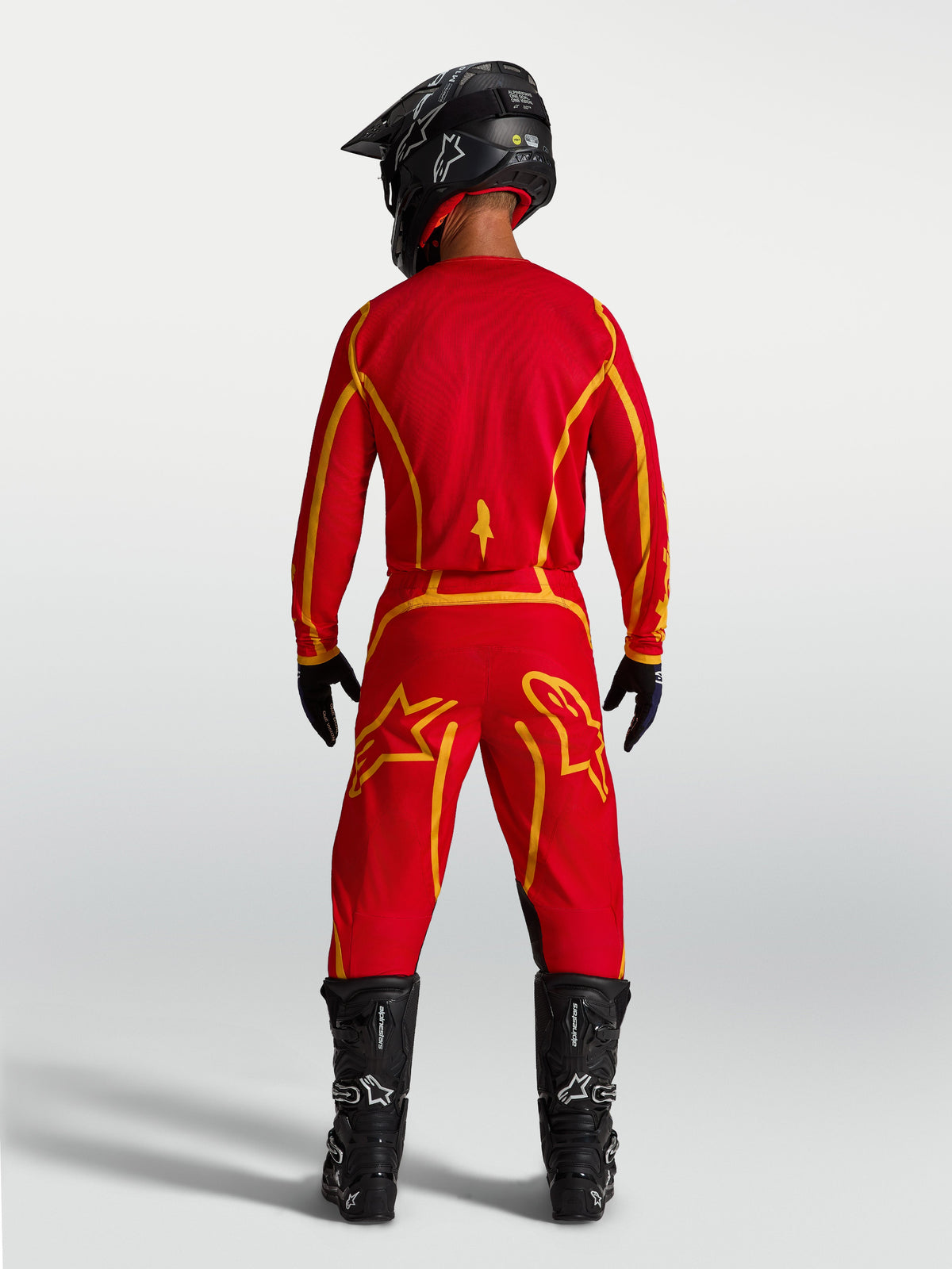 Alpinestars Pantalon Fluid Apex V2, pantalon de motocross rouge et doré, assise renforcée, vu de dos porté par un pilote.