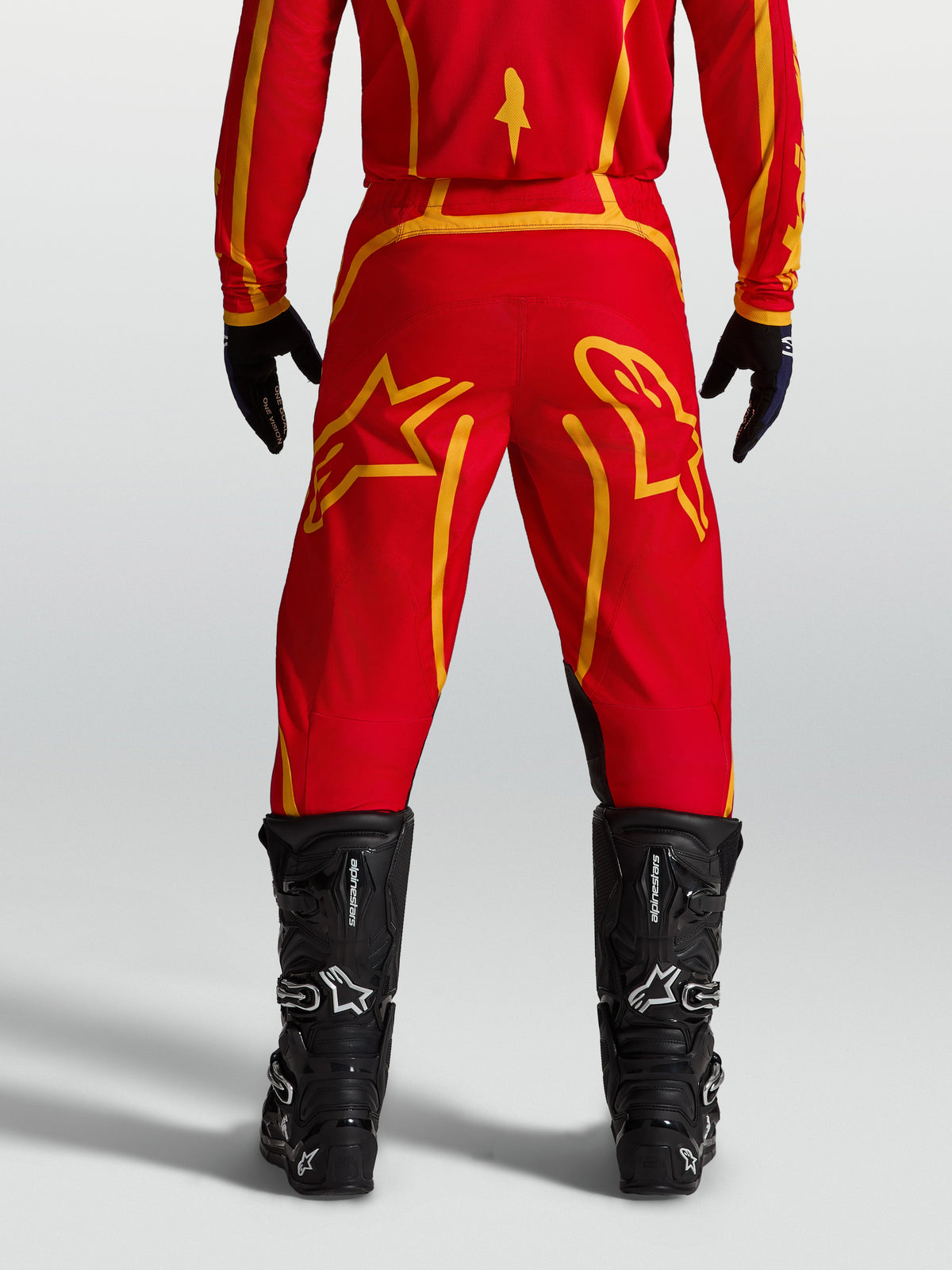 Alpinestars Pantalon Fluid Apex V2, pantalon de motocross pour homme, rouge et doré, vue de dos avec bottes noires.