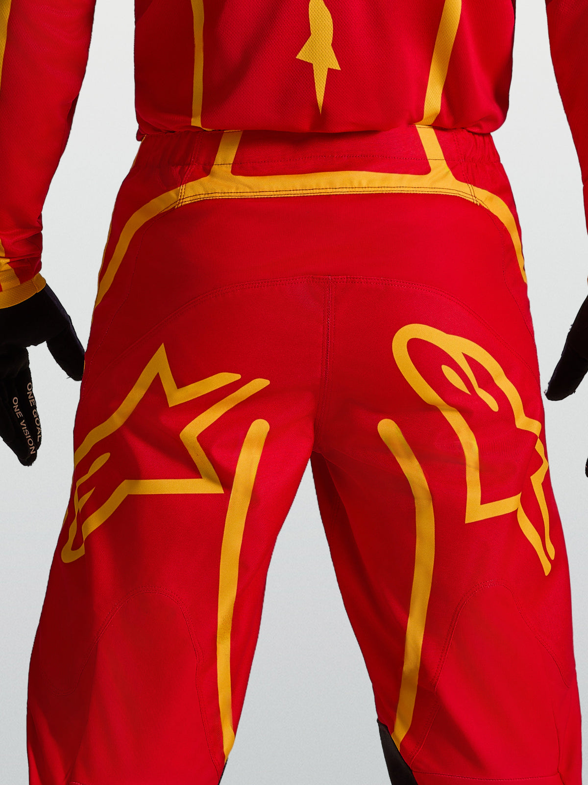Alpinestars Fluid Apex V2, pantalon de motocross rouge et doré, empiècement arrière renforcé et motifs d'étoiles.