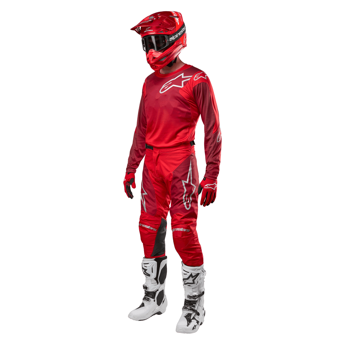 Pilote de motocross portant un équipement de course complet, pantalon et maillot Alpinestars Racer Hoen 2024 en Mars Red Burgundy, casque rouge, gants rouges et bottes blanches et noires, tenue coordonnée pour la course tout-terrain
