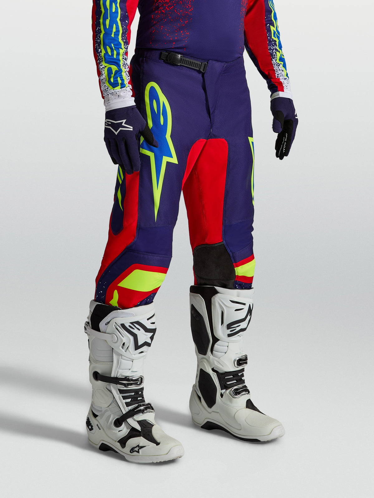 Pantalons Fluid Drag Alpinestars, équipement de motocross pour homme, bleu marine et rouge, graphismes audacieux, portés avec des bottes de moto blanches.