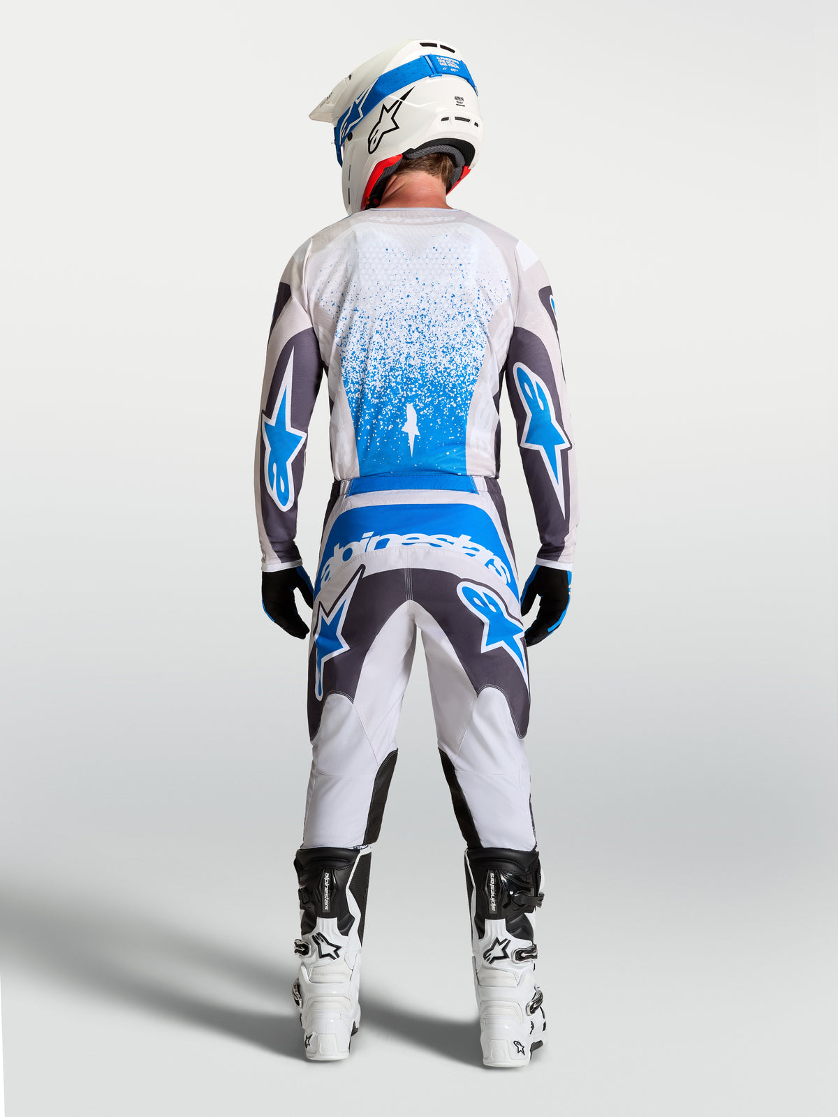 Pantalon Alpinestars Fluid Drag, pantalon de motocross tout-terrain pour homme, gris et bleu, vue de dos sur un pilote, coupe ergonomique 3D avec assise renforcée et panneaux extensibles