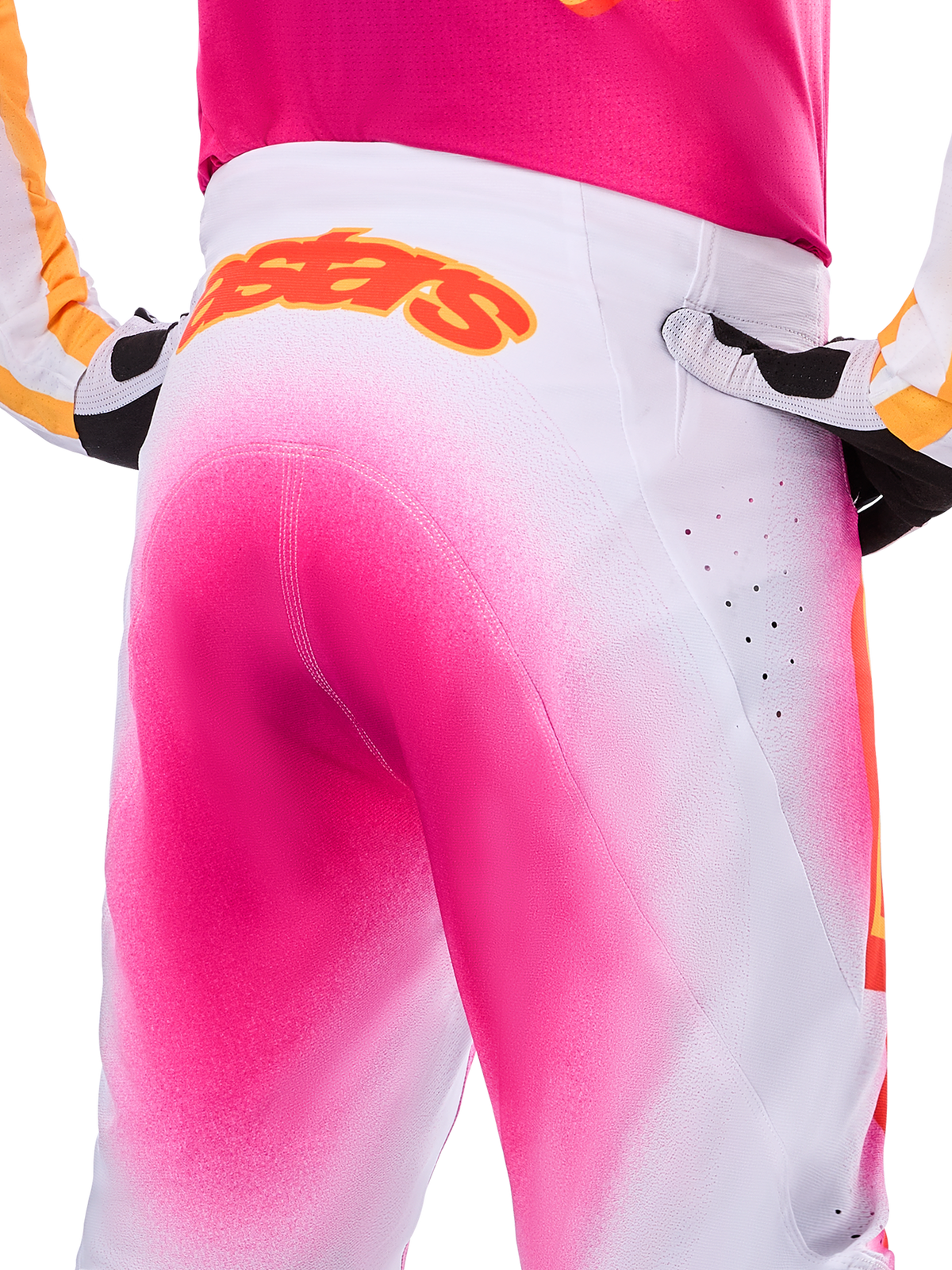Pantalon Alpinestars Supertech AFD MIG Édition Limitée, pantalon de motocross, rose fluo et blanc avec un effet de dégradé façon peinture en spray, grand logo Alpinestars orange sur la taille à l'arrière, vue rapprochée montrant la coupe athlétique et les perforations de ventilation
