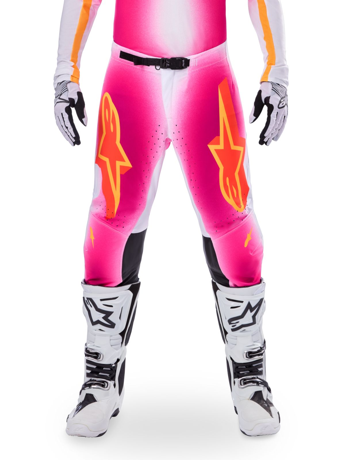 Pantalon Alpinestars Édition Limitée Supertech AFD MIG, pantalon de motocross, rose fluo et blanc avec des accents orange, avec de grands logos étoiles sur les cuisses, des panneaux perforés et des zones de préhension noires aux genoux, porté avec des bottes de motocross blanches et noires