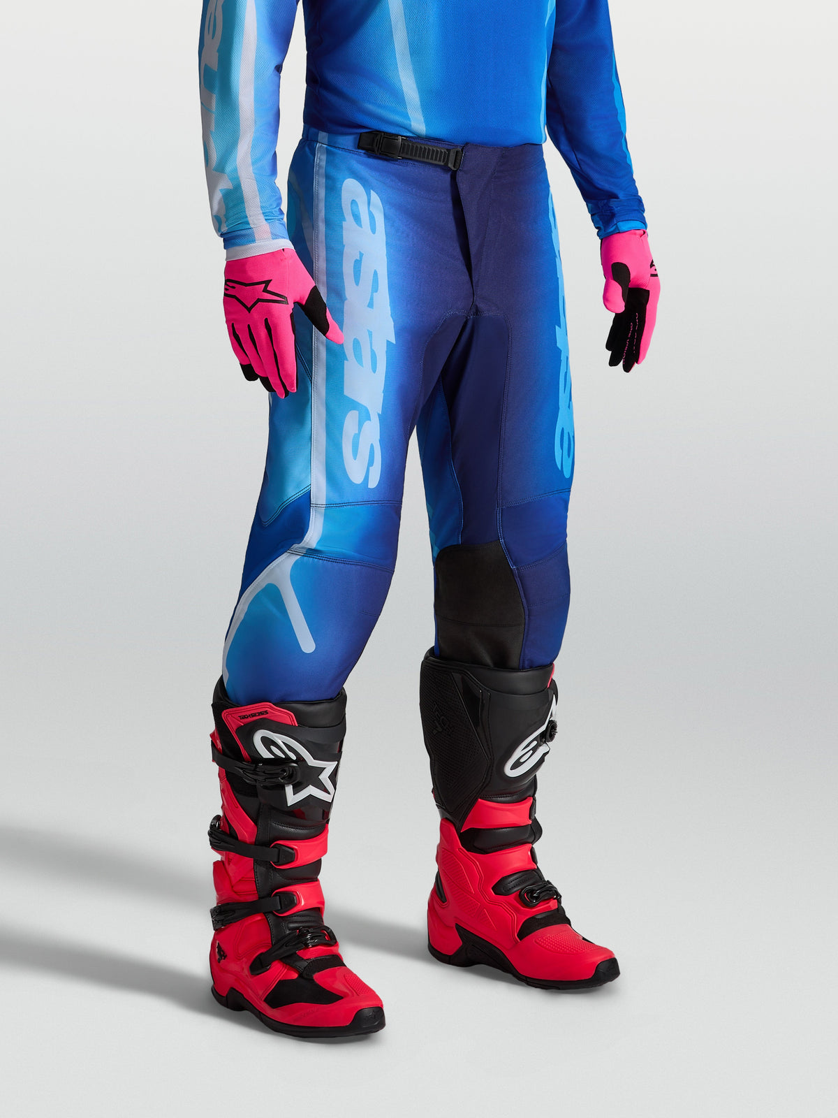 Pantalon Fluid Kepler Alpinestars, pantalon de motocross pour homme, bleu UCLA et bleu Blithe, poly-tissu 600D et jambes pré-courbées, porté avec des gants et des bottes de moto.