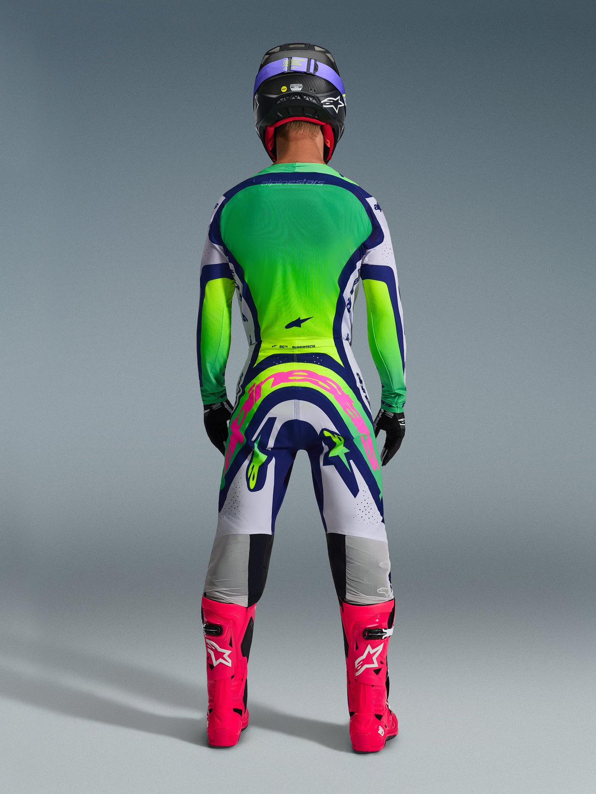 Alpinestars 2026 Supertech Vista Pants, Motocross Pants, Light Gray Yellow Fluo and Blue, rear view of rider wearing matching green and yellow gradient jersey with bright pink boots, featuring bold pink Alpinestars branding on the seat, professional athletic fit for off-road racing.