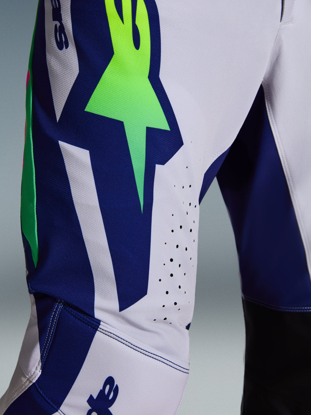 Alpinestars 2026 Supertech Vista Pants, pantalon de motocross, gris clair avec accents jaune fluo et bleu, vue rapprochée de la cuisse montrant le grand logo A-star, perforations laser et tissu rip-stop extensible de pointe.