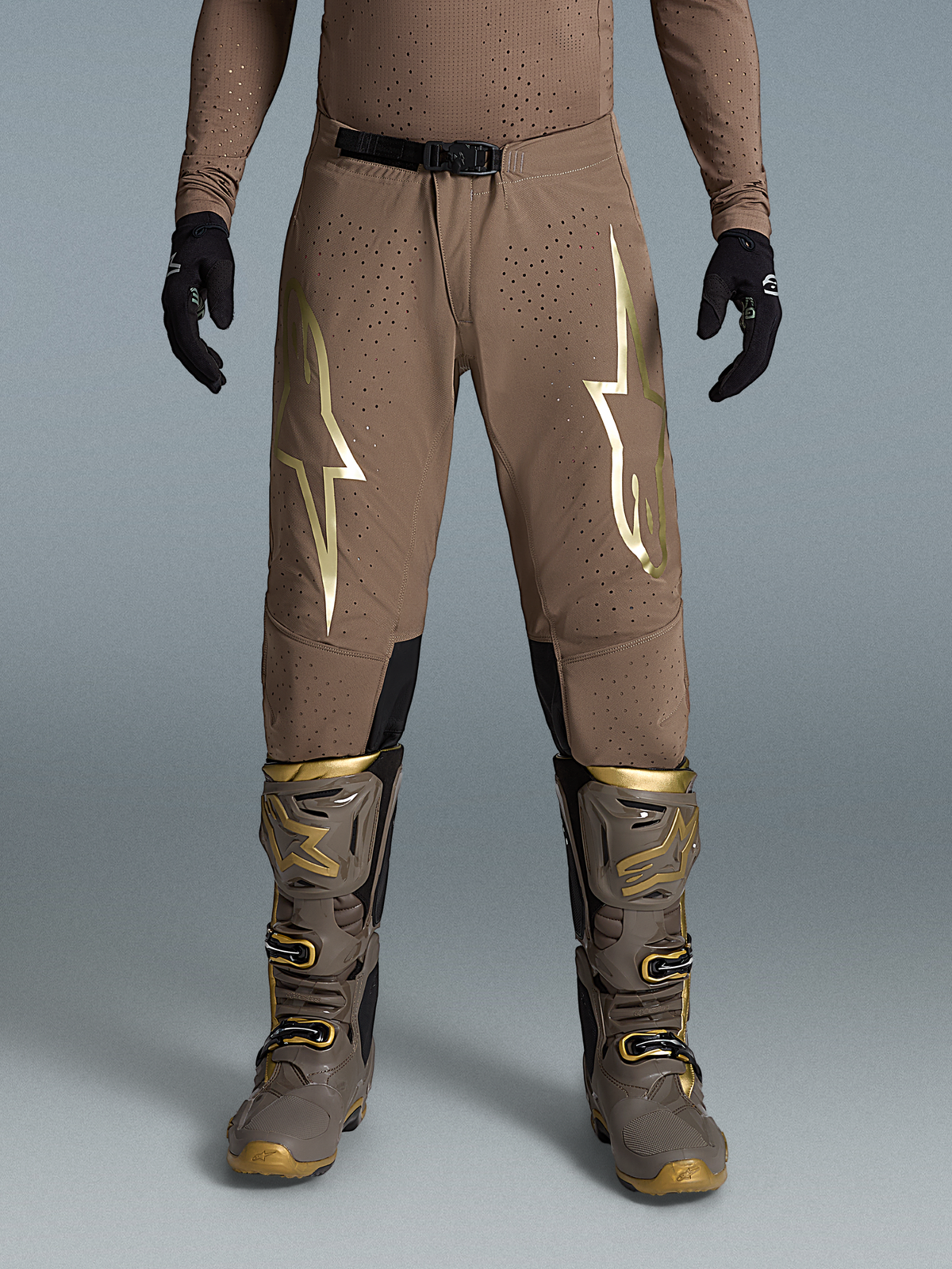 Alpinestars Pantalon Supertech Air Gold Édition Limitée, pantalon de motocross tout-terrain, marron et doré, tissu rip-stop ventilé, porté avec bottes et gants par un mannequin