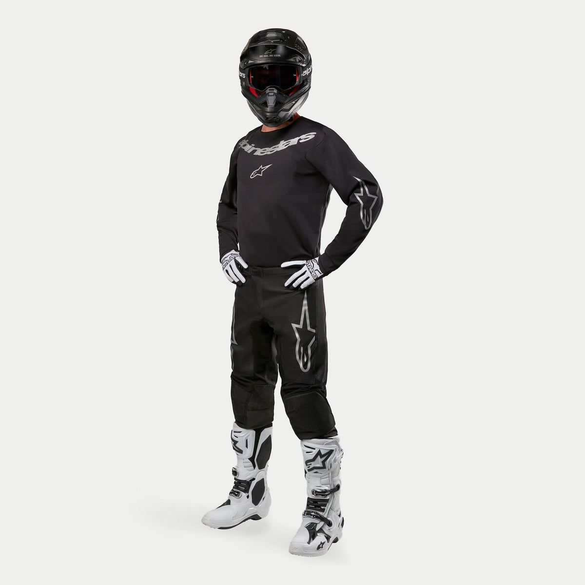 Alpinestars 2024 Fluid Graphite Pants, Motocross Pants, Black and Silver, worn with matching black jersey, black helmet, white gloves, and white boots, featuring silver Alpinestars logos on the thighs, ergonomic athletic fit for off-road racing.