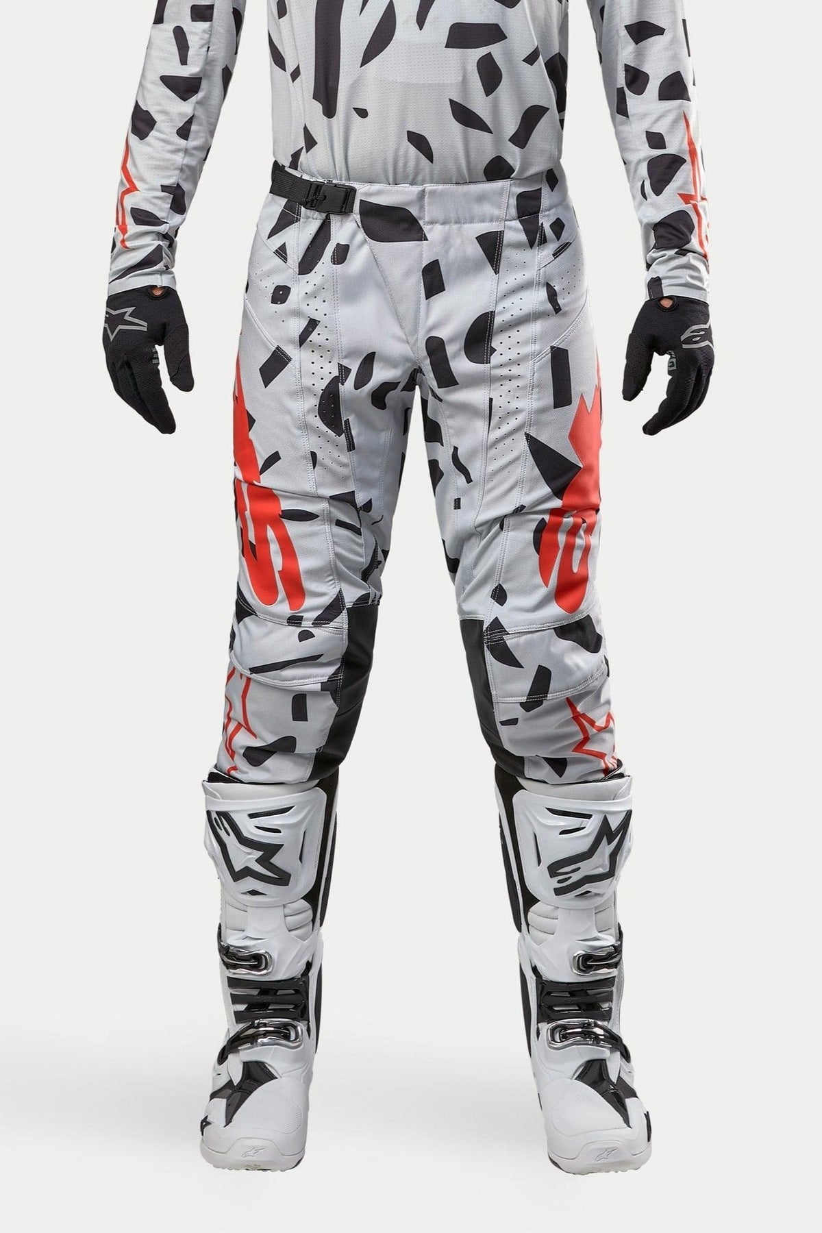 Pantalon Alpinestars Techstar Rantera 2024, pantalon de motocross, Haze Gray Camo, porté avec un maillot assorti, des gants noirs et des bottes blanches, avec des motifs à taches noires et logos Alpinestars rouges, conception durable pour la course tout-terrain