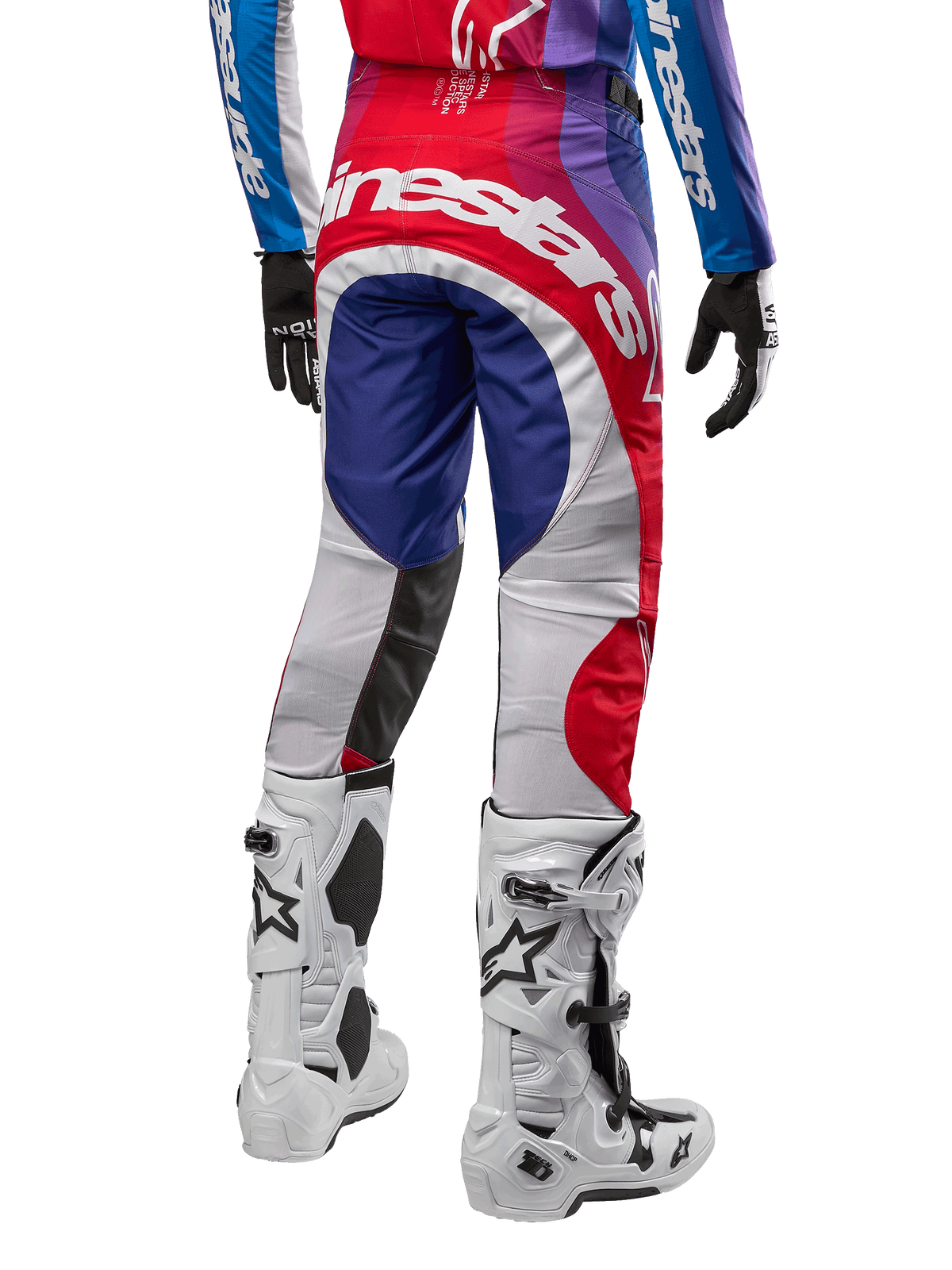 Alpinestars Pantalon Techstar Pneuma 2024, pantalon de motocross, bleu, rouge et blanc, vue arrière porté avec maillot assorti et bottes blanches, logo blanc imposant sur l'assise et empiècements multicolores, équipement de course professionnel