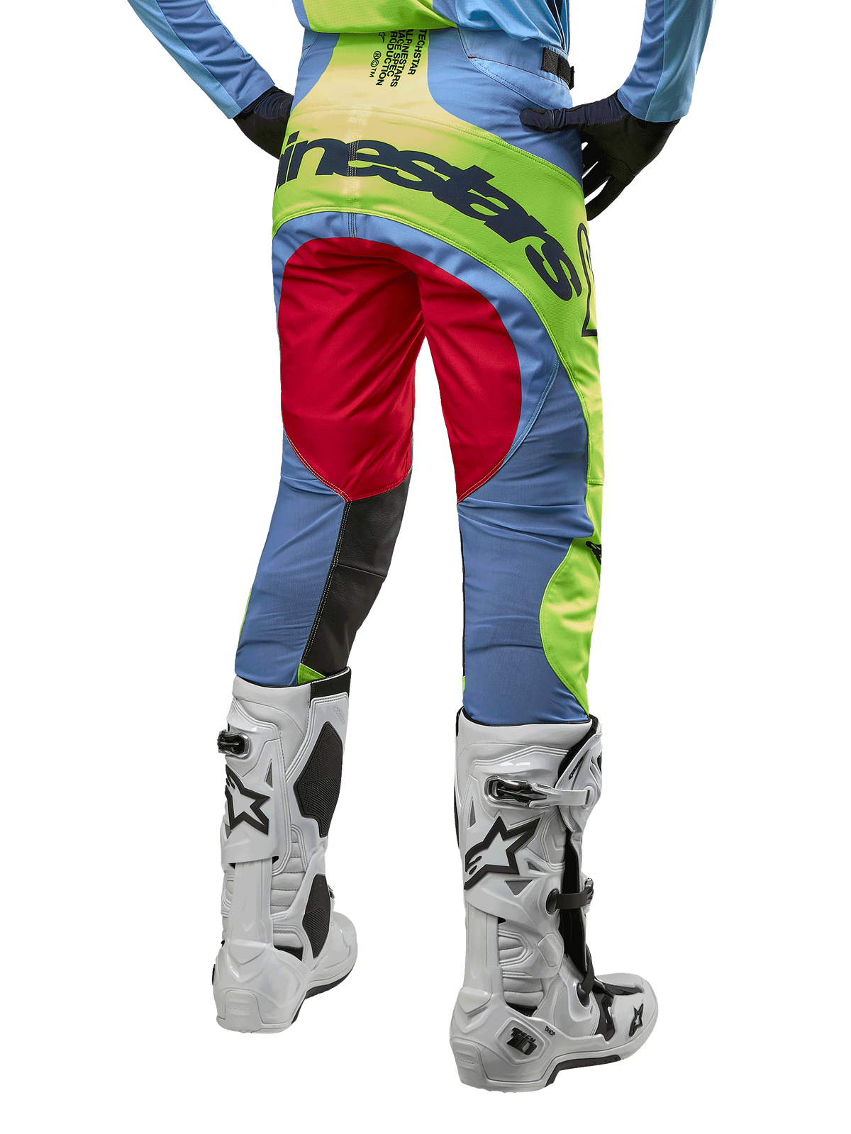 Alpinestars Techstar Ocuri Pants 2024, pantalon de motocross, bleu clair, jaune fluo et rouge, vue de dos porté avec des bottes de motocross blanches et noires, avec un color-block éclatant et le logo Alpinestars sur l'assise.