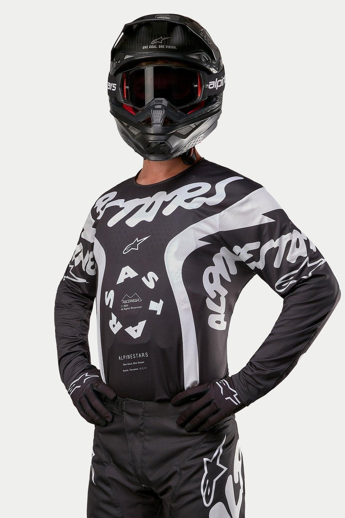 Alpinestars 2024 Racer Hana Jersey, maillot de motocross, noir et blanc, avec des graphismes et un logo Alpinestars blancs audacieux, porté par un pilote avec un casque et des lunettes noirs, équipement haute performance pour la course tout-terrain