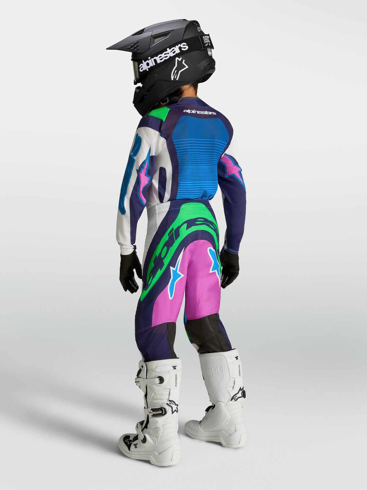 Alpinestars pantalon Supertech Maven Junior, pantalon de motocross bleu, rose et vert pour enfant, construction ripstop légère, vue de dos sur un pilote avec bottes blanches