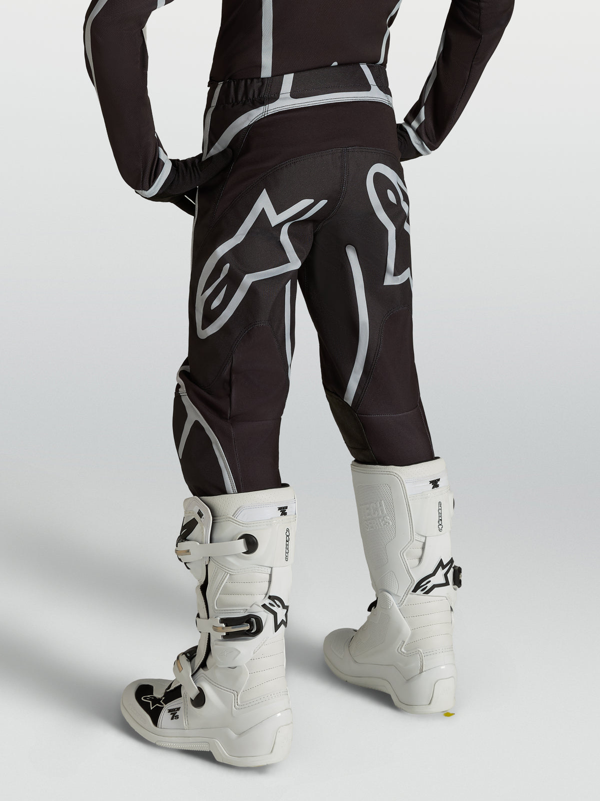 Alpinestars Pantalon Fluid Apex V2 Junior, pantalon de motocross pour enfant, noir et argenté, vue de dos avec bottes blanches