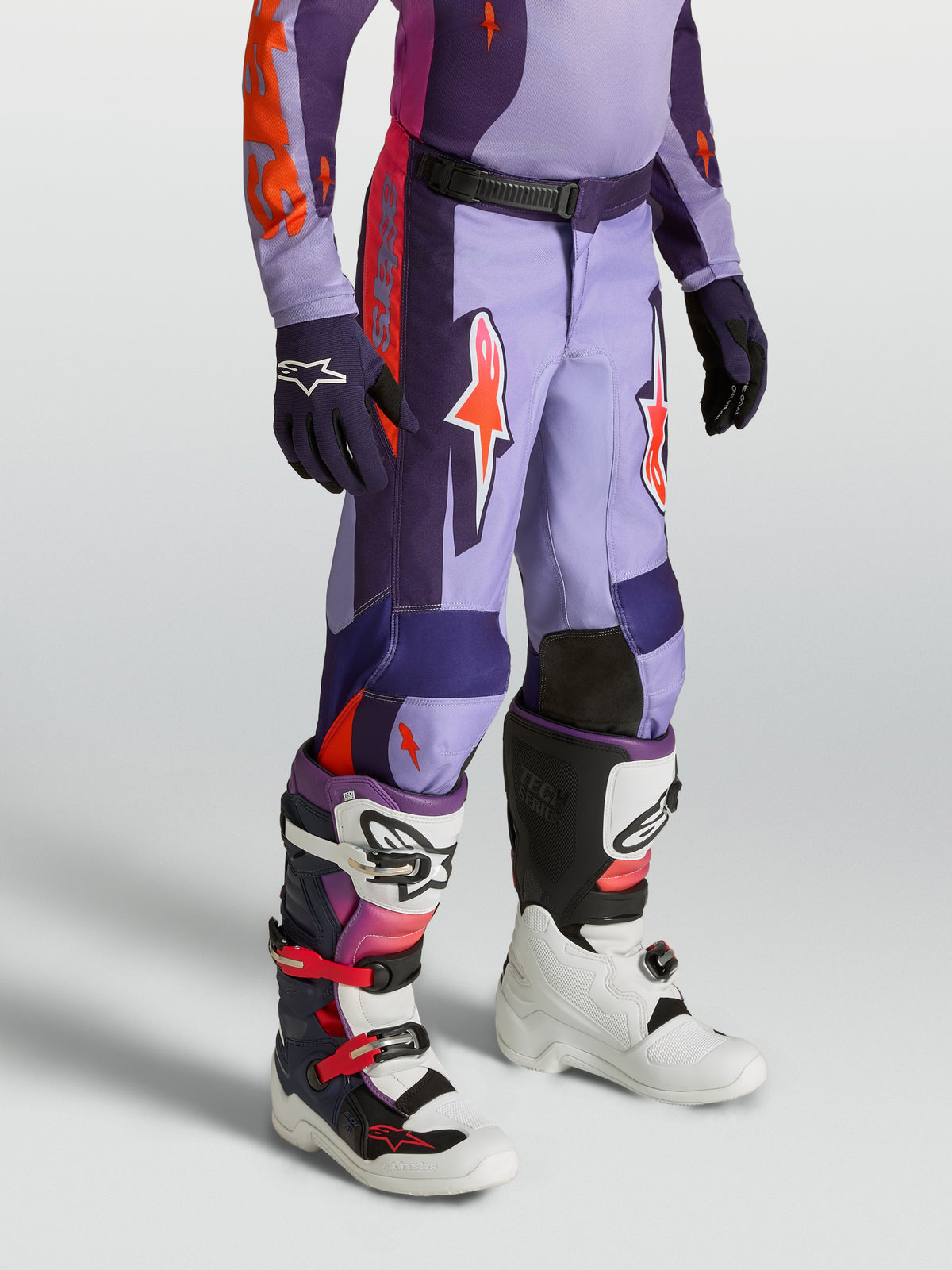 Alpinestars Pantalon Fluid Hunt Junior, pantalon de motocross enfant violet et rose, coupe sport, porté avec des bottes.