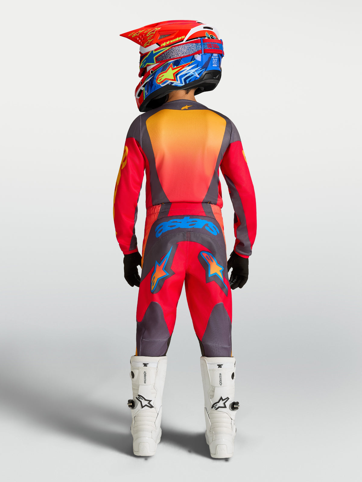 Pantalons de motocross Alpinestars Fluid Hunt Junior 2027 rouges et gris, vue arrière d'un jeune pilote avec bottes blanches