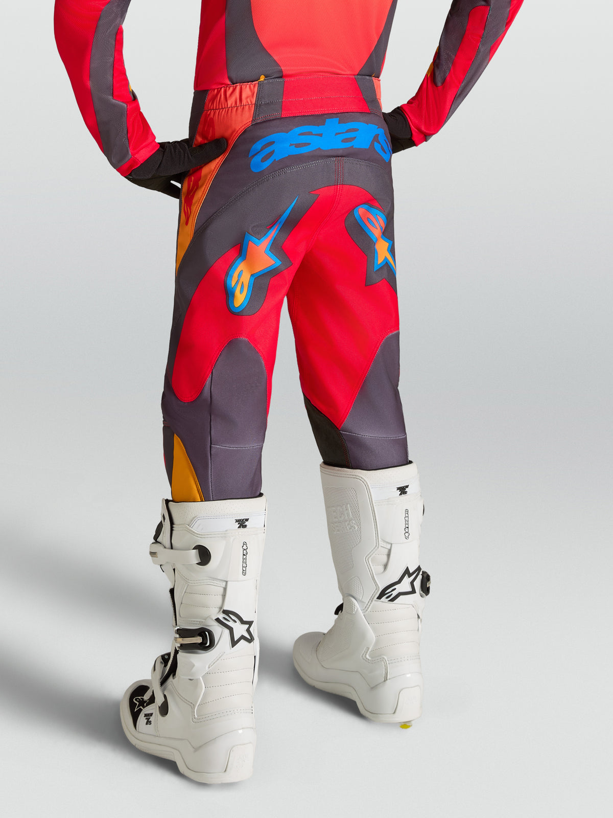 Pantalons Alpinestars Fluid Hunt Junior, pantalons de motocross pour enfant, rouges et gris, vue de dos avec assise renforcée en 600D, portés avec des bottes de moto blanches