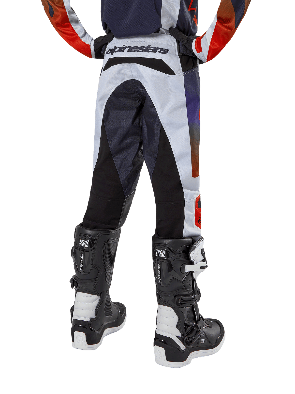 Alpinestars Pantalon Racer Hoen Junior 2024, pantalon de motocross, gris clair avec accents orange vif et noirs, vue arrière présentant des panneaux noirs sur l'assise et les jambes, logo distinctif à la taille, porté avec des bottes de motocross noires et blanches pour la course tout-terrain