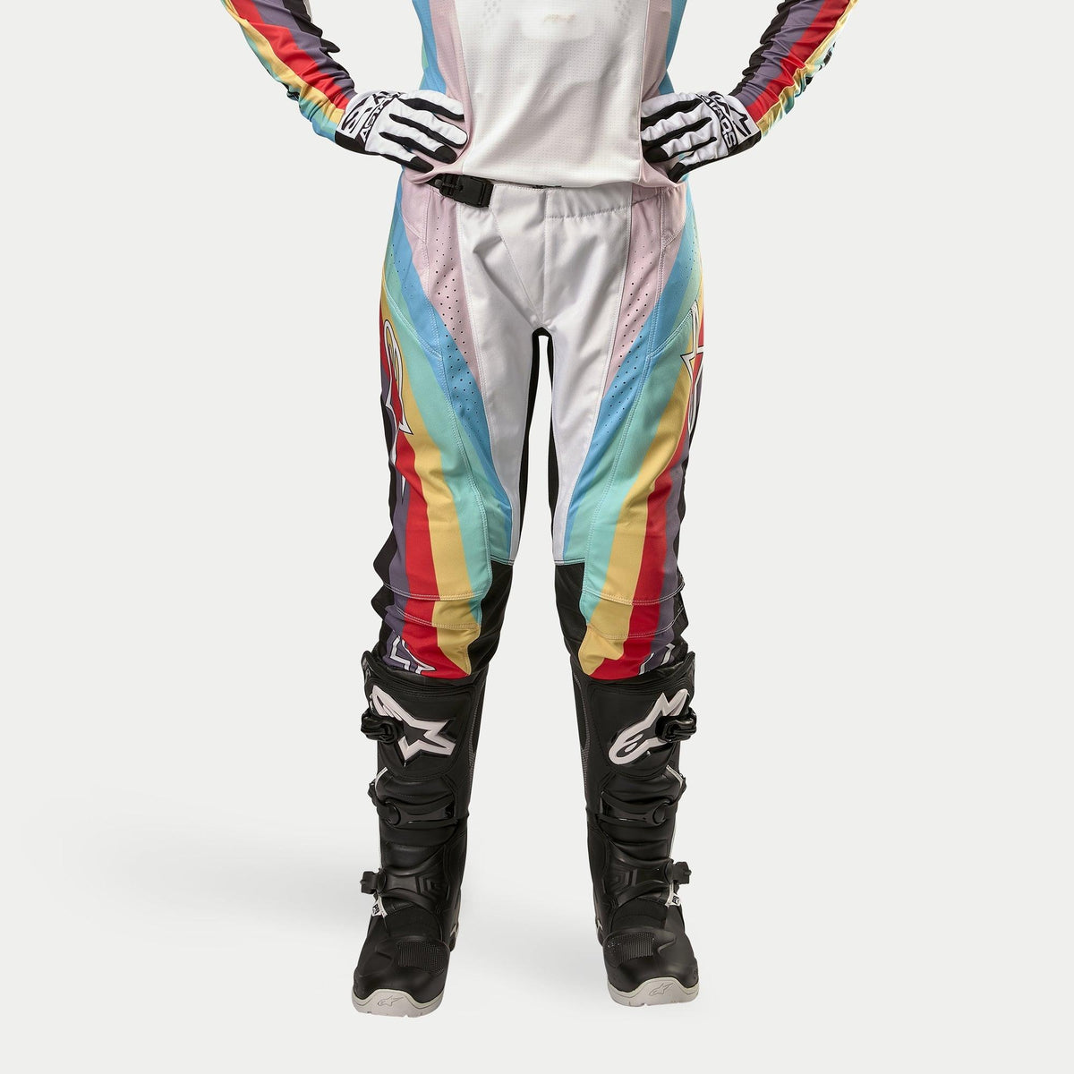 Alpinestars Stella Techstar Pants 2024 pour femme, pantalon de motocross, noir multicolore, avec des rayures diagonales vives en blanc, bleu, rouge et jaune, porté avec des bottes et des gants de motocross noirs, design inspiré de la course pour la performance tout-terrain.