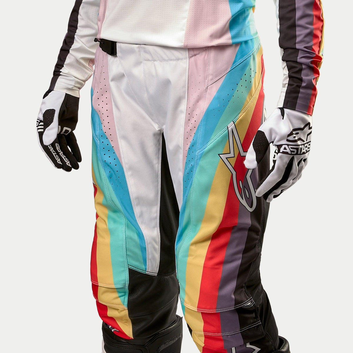 Alpinestars Pantalon Femme Stella Techstar 2024, pantalon de motocross, noir multicolore avec des rayures diagonales vives en bleu, rose, jaune et rouge, doté d'un grand logo étoile sur la cuisse, présenté avec le maillot et les gants assortis, équipement de course tout-terrain professionnel