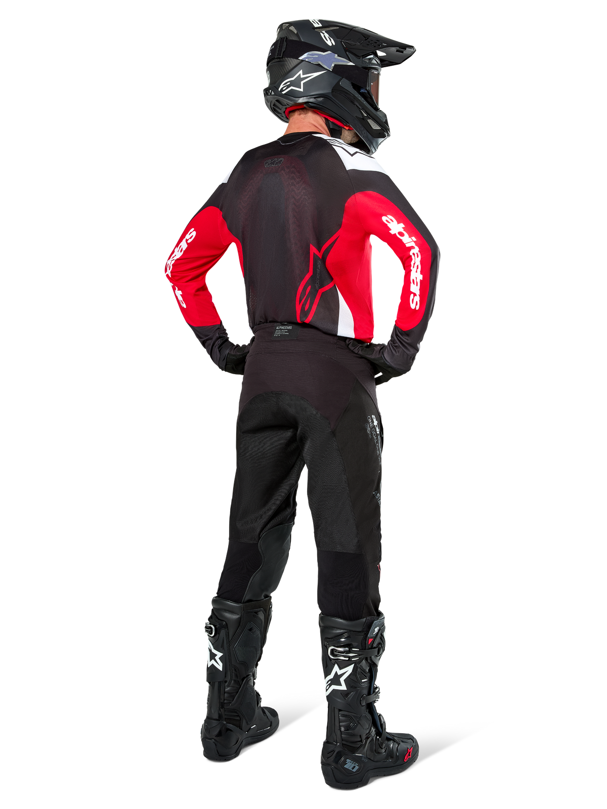 Pilote de motocross vu de dos portant le maillot Alpinestars Pro-Dura noir, rouge vif et blanc, avec pantalon, casque et bottes noirs, montrant le design arrière et les logos sur les manches, équipement de course tout-terrain coordonné