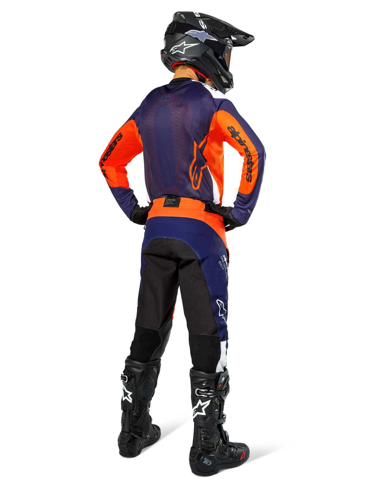 Pilote de motocross de dos portant le maillot Alpinestars Pro-Dura, bleu marine, orange vif et blanc, pantalon assorti bleu marine et orange, casque noir et bottes noires, doté d'un panneau arrière en mesh respirant et d'un dos allongé, équipement coordonné pour l'enduro