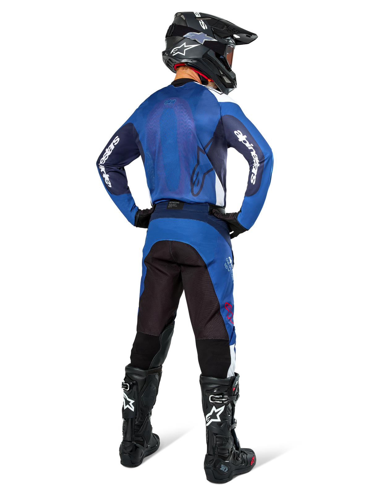 Pilote de motocross vu de dos portant le maillot Alpinestars Pro-Dura en bleu marine et bleu vif, avec pantalon bleu et noir assorti, casque de motocross noir avec lunettes et bottes noires, présentant une tenue de course tout-terrain coordonnée