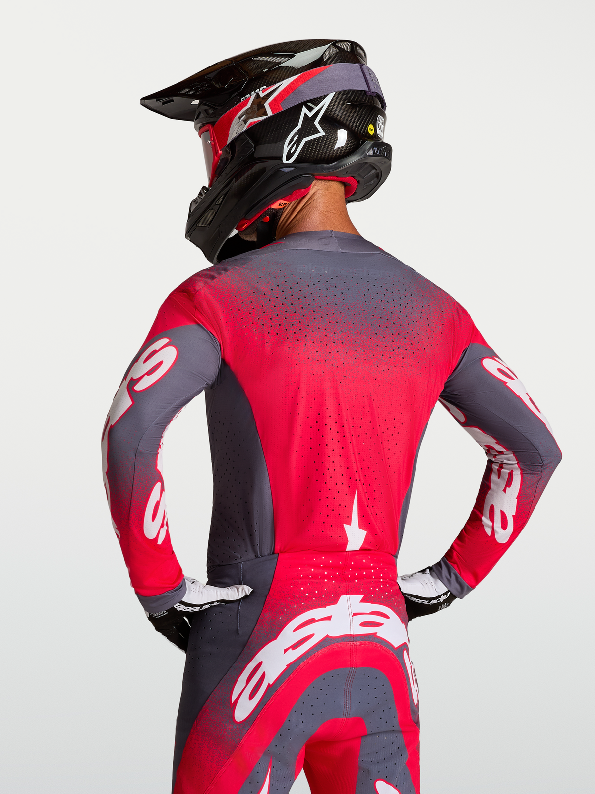 Maillot Supertech Hiten AFD Alpinestars, maillot de motocross gris et rouge fluo, vue de dos montrant la ventilation Stretchnet et la coupe racing athlétique sur un pilote.