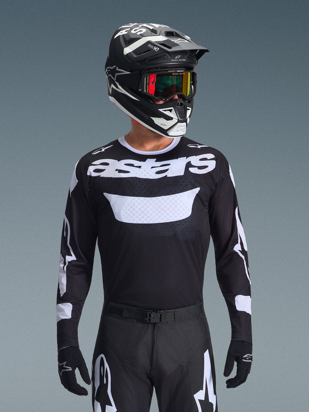 Pilote de motocross portant l'ensemble d'équipement Alpinestars Racer Air Riway 2026, maillot noir avec logo 'astars' blanc et panneau de poitrine ventilé, pantalon noir avec accents blancs, casque noir et blanc assorti avec lunettes irisées, gants noirs, équipement de motocross haute performance noir et blanc.