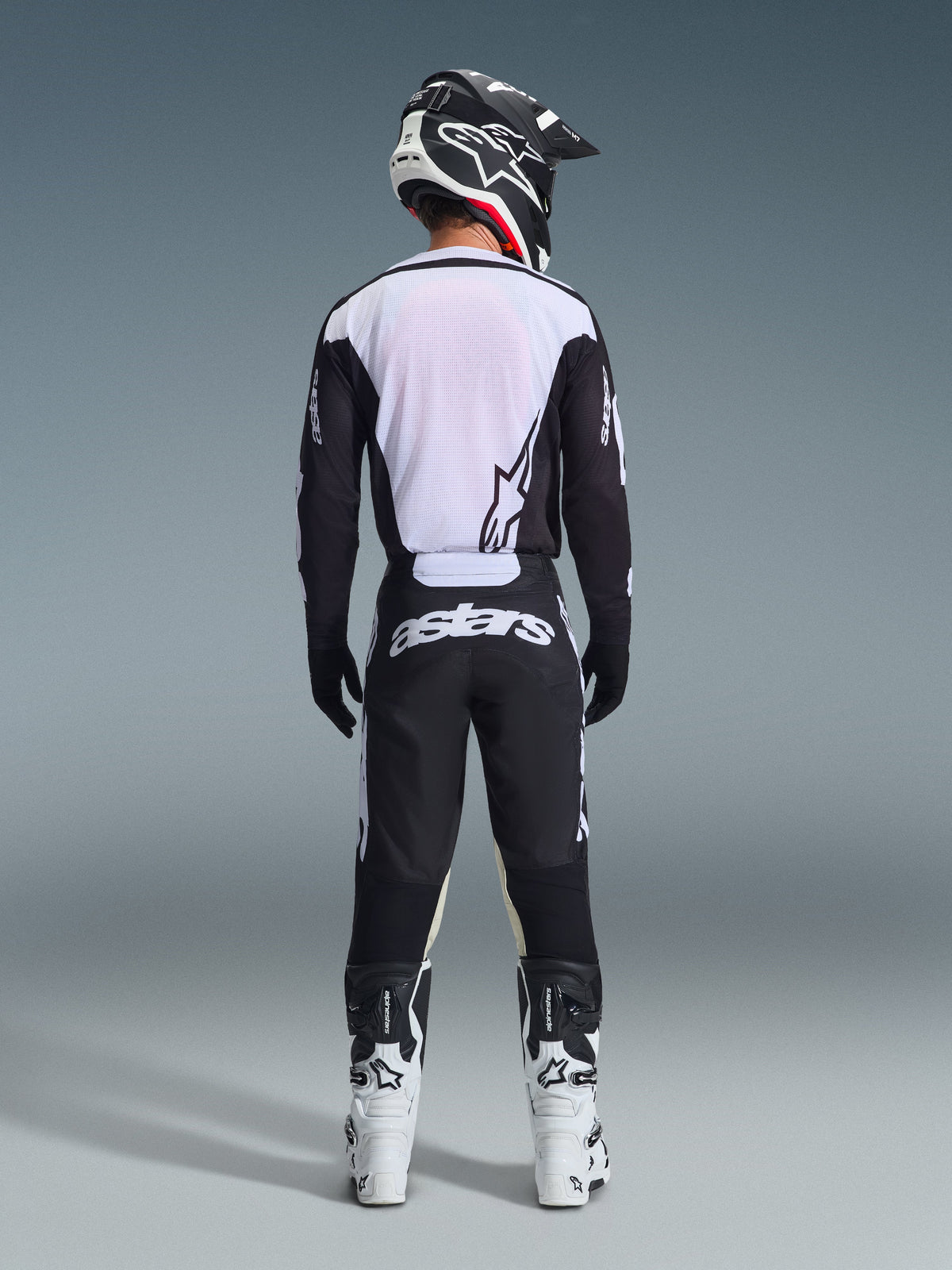 Set d'équipement Alpinestars Racer Air Riway 2026, équipement de motocross, noir et blanc, vue arrière d'un pilote portant un maillot ventilé avec panneaux en mesh blanc, pantalon assorti avec marquage astars sur l'assise, coordonné avec des bottes et un casque de motocross blancs et noirs
