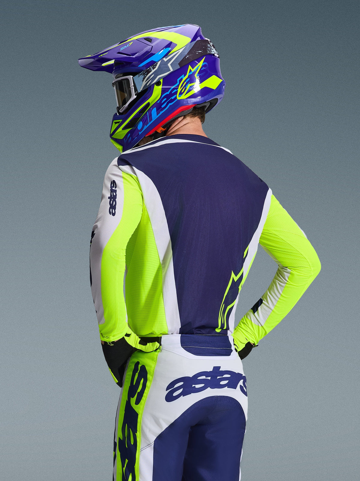 Alpinestars 2026 Racer Air Riway Jersey, maillot de motocross, gris clair, jaune fluo et bleu, vue arrière d'un pilote portant un pantalon et un casque assortis, coupe sportive avec panneaux en maille respirante pour la course tout-terrain