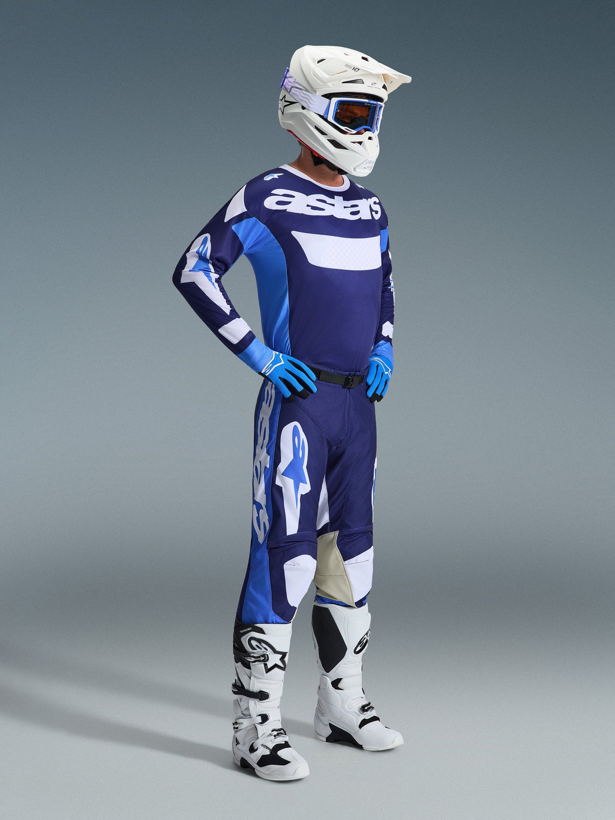 Motocross rider wearing the Alpinestars 2026 Racer Riway Gear Set in UCLA Blue and White, featuring a blue and white jersey with 'astars' branding, matching pants, a white helmet with blue goggles, and white off-road boots, complete racing outfit for motocross.