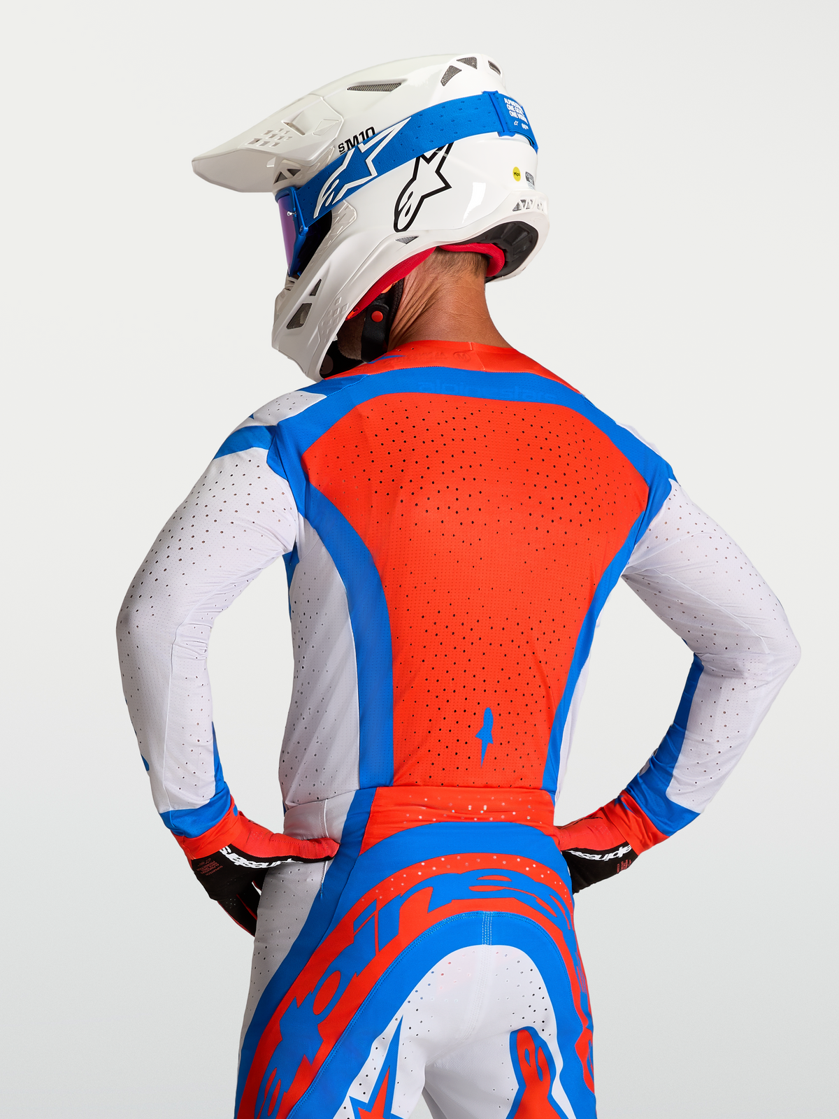 Alpinestars Maillot Supertech Vesta, maillot de motocross pour homme, rouge, bleu et blanc, avec perforations laser respirantes, vue de dos sur un mannequin avec casque, équipement de performance tout-terrain