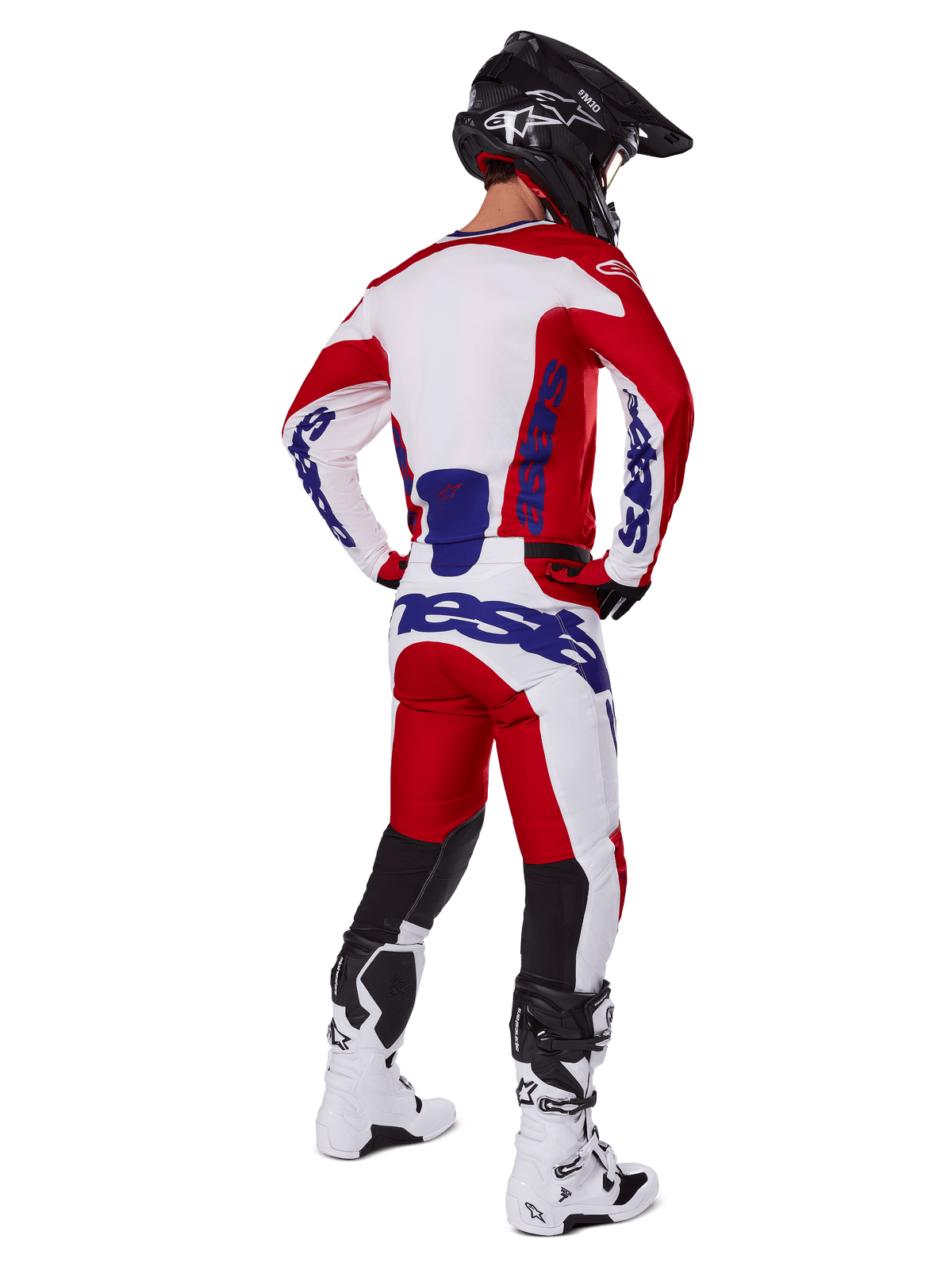 Pilote de motocross vu de dos portant le maillot et le pantalon Alpinestars Racer Veil 2025 en rouge et blanc, avec logos bleus, casque noir et bottes blanches, tenue complète pour la course tout-terrain