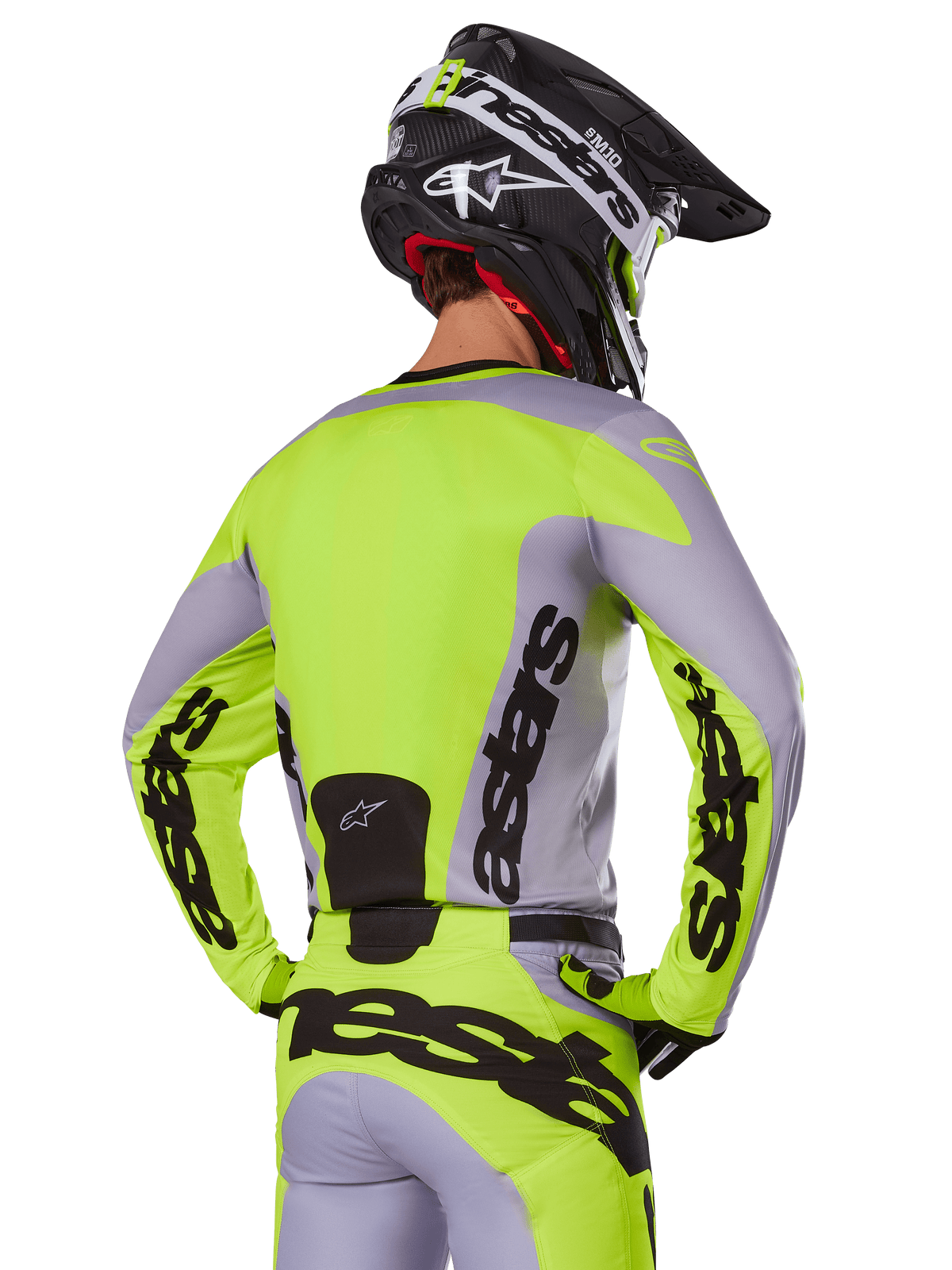 Pilote de motocross de dos portant le maillot Alpinestars Racer Veil 2025 en gris et jaune fluo, avec marquage 'astars' distinctif au dos et sur les manches, assorti d'un pantalon coordonné et d'un casque noir pour un look de course complet.