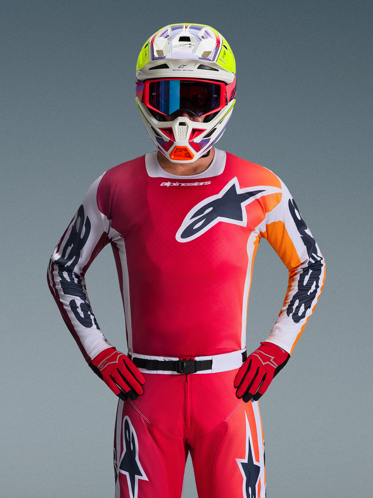 Alpinestars 2026 Racer Portl Gear Set, Motocross rider wearing a vibrant red jersey with orange and white accents, matching red pants and gloves, multi-colored helmet with neon yellow highlights and blue goggles, large star logo on chest, professional off-road racing gear