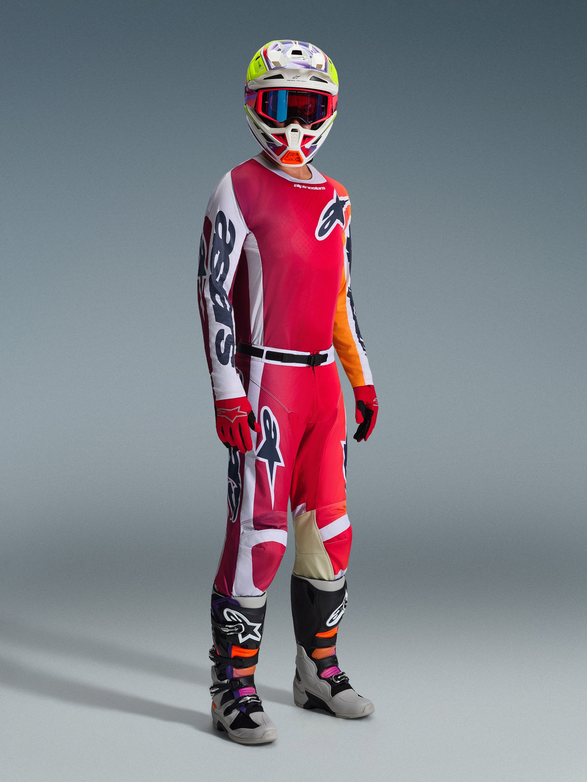 Motocross rider wearing the Alpinestars 2026 Racer Portl Gear Set, featuring a Red and White jersey with bold 'Astars' branding on the sleeve, matching Red and White pants, a coordinated white and yellow helmet with red-framed goggles, and gray and black motocross boots, complete outfit for off-road racing.