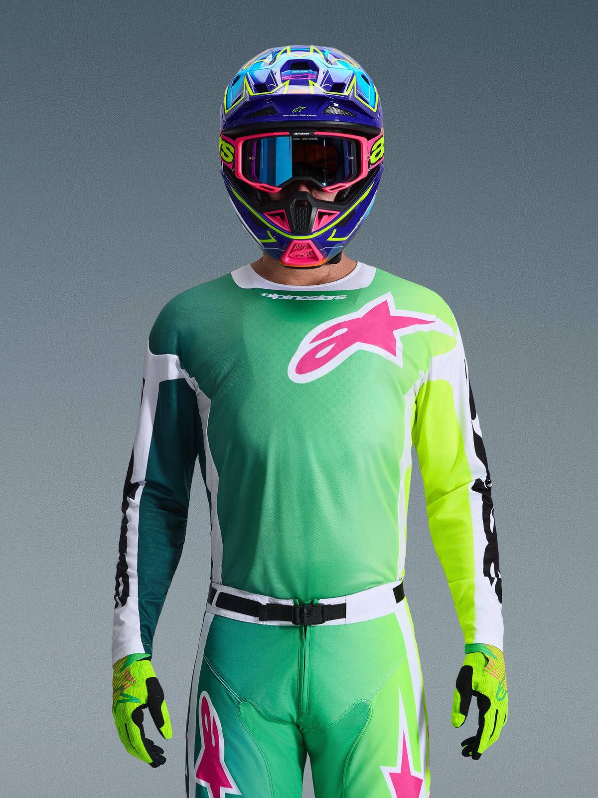 Set d'équipement Alpinestars Racer Portl 2026, pilote de motocross portant un maillot avec dégradé vert et jaune et logo Astars rose, pantalon assorti, casque bleu et rose avec lunettes bleues, et gants vert citron, tenue de course tout-terrain professionnelle coordonnée